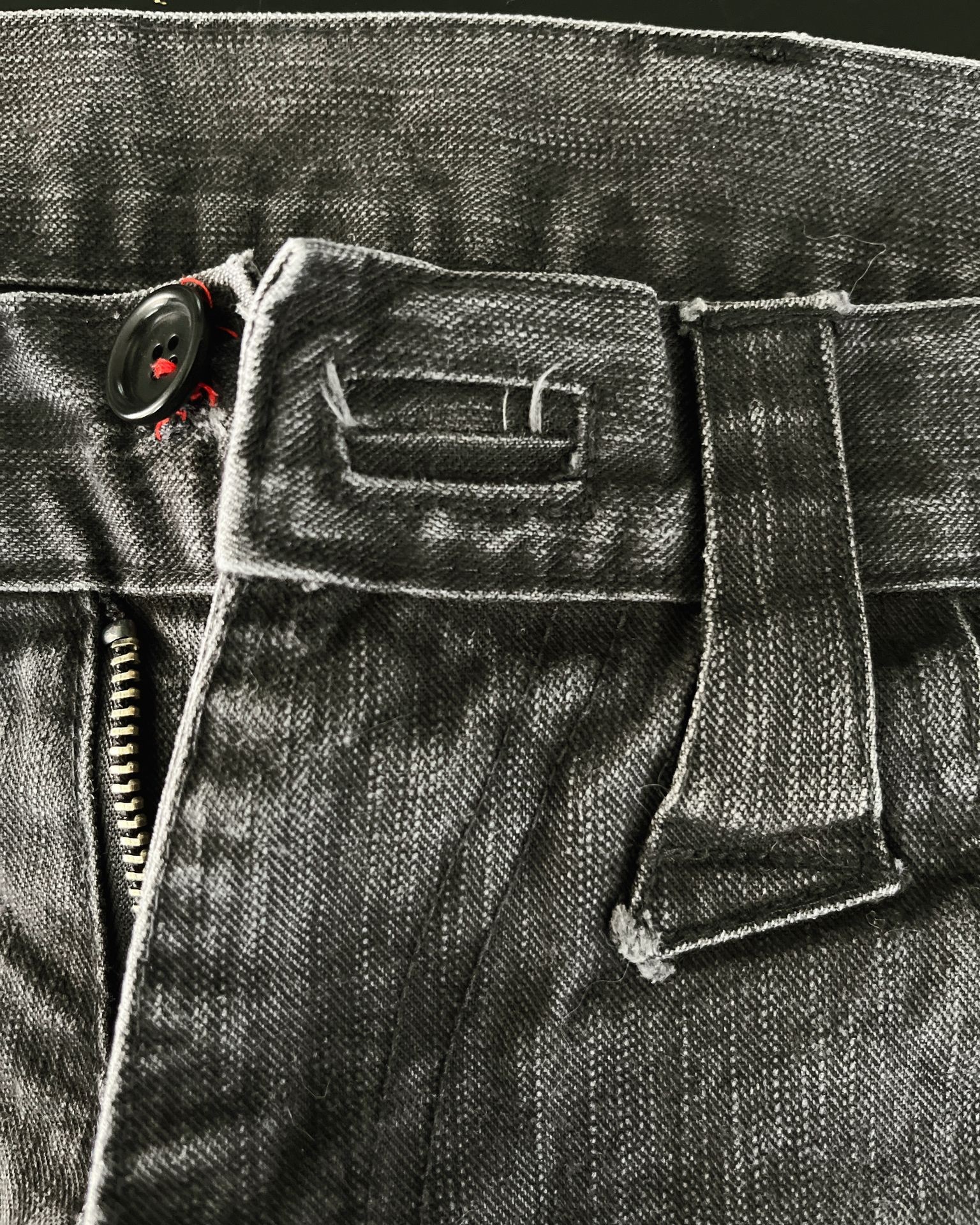 Close-up of a black denim jeans waistband with a button, belt loop, and zipper.