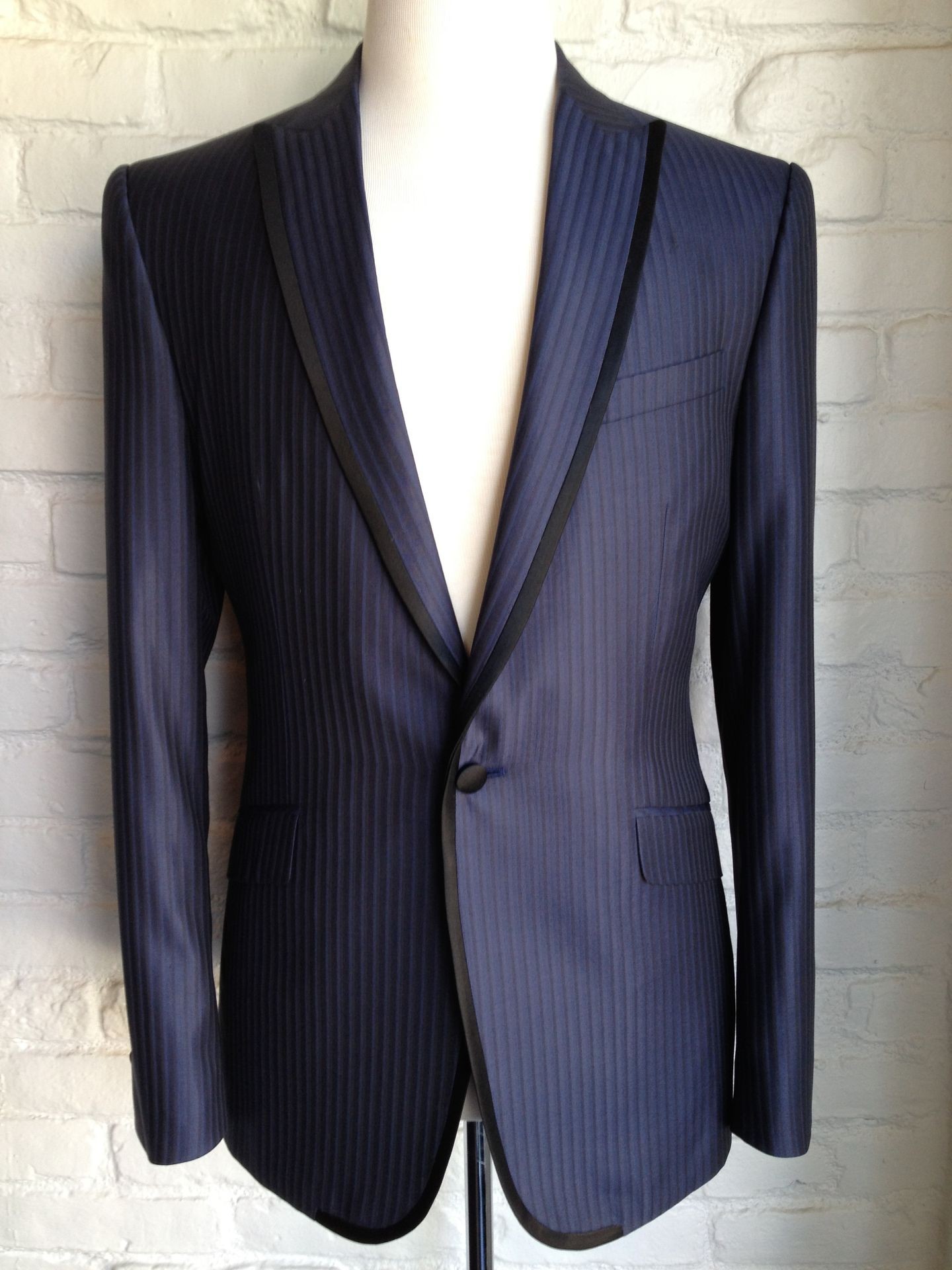 A navy blue pinstripe blazer with black trim on a display mannequin against a white brick wall.